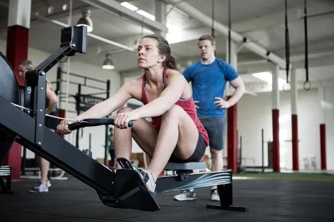 Woman Using Rowing Machine While Instructor Standing By 写真素材