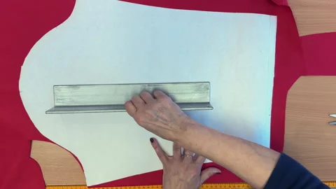 Woman using ruler to cut fabric pattern on red textile surface Stock Footage 345679447