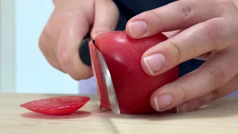 Woman using a sharp knife to cut a red tomato on a wooden cutting board in a Stock Footage 316456752