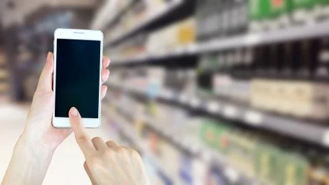 Woman using smart phon while shopping in supermarket Stock Photos