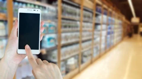 Woman using smart phon while shopping in supermarket Stock Photos