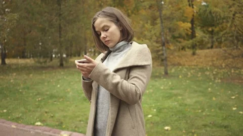 Woman using smart phone while standing in autumn park Stock Footage 132284961