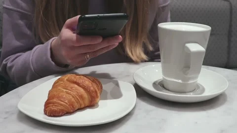 Woman using smart phone while sitting at cafe with coffee and croissant Stock Footage 221785227