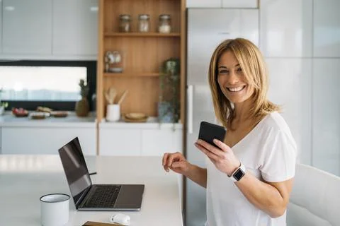 Woman Using Smart phone While Sitting at Kitchen Table Foto stock
