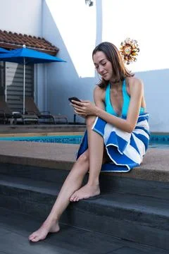 Woman using smart-phone while wrapped in towel at poolside Stock-Fotos