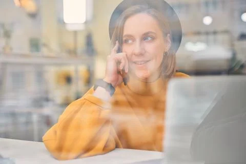 Woman using smart phone while working on laptop at cafe Stock Photos