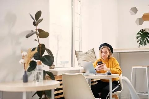 Woman using smart phone while working on laptop at cafe Stock Photos