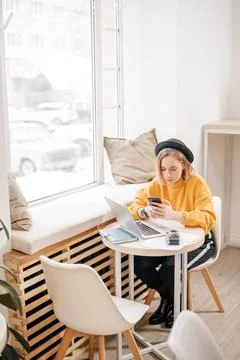 Woman using smart phone while working on laptop at cafe Stock Photos