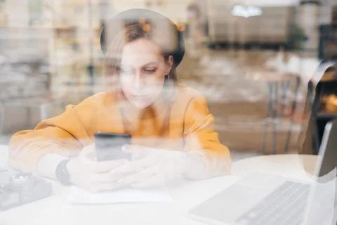 Woman using smart phone while working on laptop at cafe Stock Photos