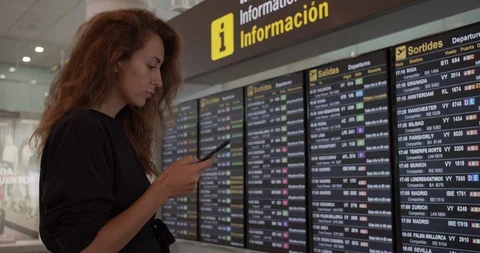 Woman using smartphone at airport. Young caucasian traveler checking boarding Stock Footage