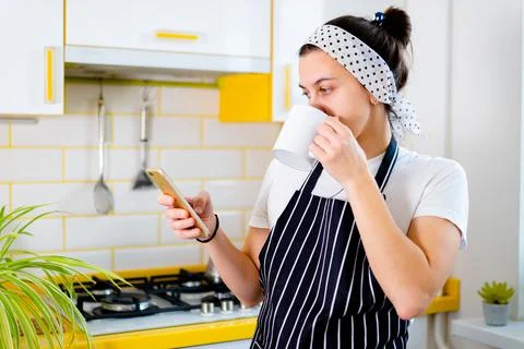 Woman using smartphone and drinking coffee in kitchen. Concept happy morning Stock Photos