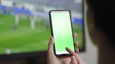 A woman using a smartphone.In the background, a screen with a football match Stock Footage 152165621