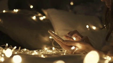 Woman using Smartphone on  the bed. Using phone, social networking. Christmas Li 스톡 동영상 98953086