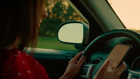 Woman using smartphone behind steering wheel at car, increasing risk of road Stock Footage 303433315
