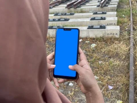 Woman using smartphone with blank screen on railway tracks. Blue screen. Stock Photos