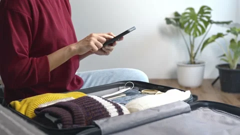 Woman using smartphone checklist getting ready for travel, packing clothes an Stock Footage 195298568