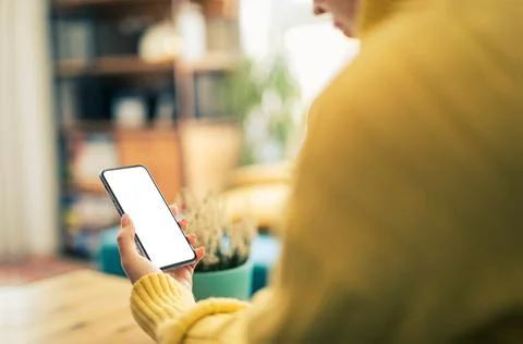Woman using smartphone frameless mockup blank screen in home interior. Workin Stock Photos