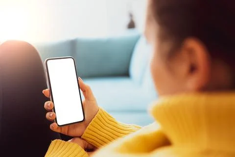 Woman using smartphone frameless mockup blank screen in home interior. Workin Stock Photos