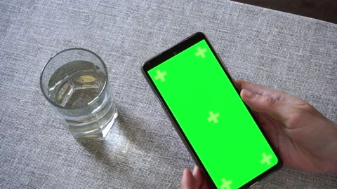 Woman using smartphone with green screen and drinking water at table, close up Stock Footage