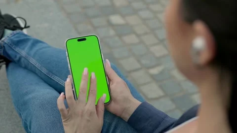 Woman Using Smartphone with Green Screen Mock-up and Headphones On City Park Stock Footage 341864800