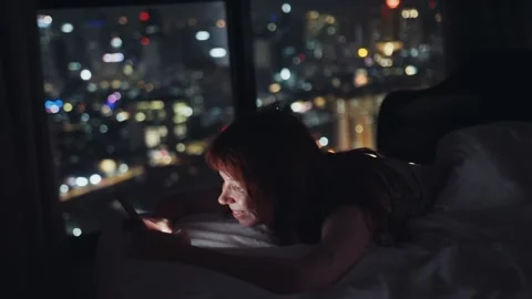 Woman using smartphone lying on bed in hotel room at night Stock Footage 302161757