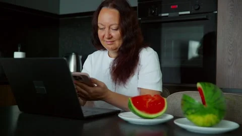 Woman using smartphone in modern kitchen with fresh watermelon Stockbeeldmateriaal 339631999
