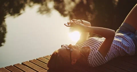 Woman using smartphone outdoors, smiling and relaxing on a wooden jetty near the 스톡 동영상 51070751