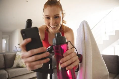 Woman using smartphone while exercising on stationary bike at home Stock Photos