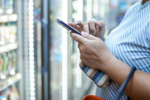 Woman Using Smartphone While Grocery Shopping in Supermarket Aisle Stock Photos
