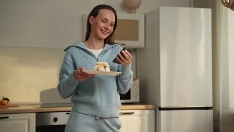 Woman using a smartphone while having breakfast at the kitchen table. A woman 스톡 동영상 262631363