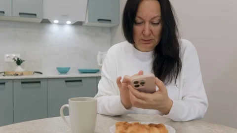 Woman using smartphone while having breakfast in kitchen Stock Footage 306432952