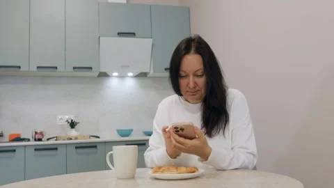 Woman using smartphone while having breakfast in modern kitchen Stock Footage 306634888