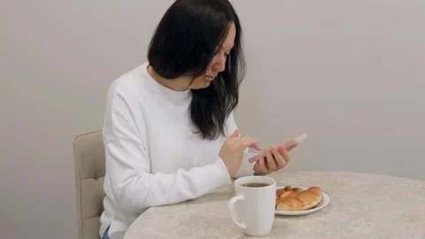 Woman using smartphone while having breakfast at home Stock Footage 307156694