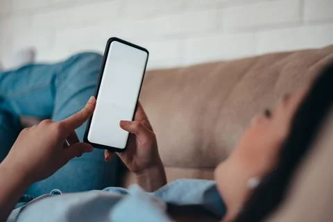 Woman using smartphone while lying on the couch at home Stock Photos