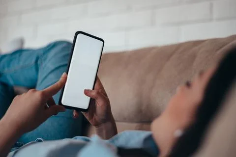 Woman using smartphone while lying on the couch at home Stock Photos