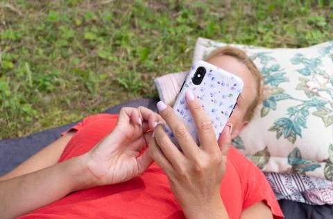 Woman Using Smartphone While Lying Outdoors on Grass with Pillow Stock Photos