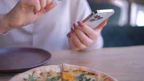 A woman is using a smartphone while a pizza is placed on the table in front of Stock Footage 276680143