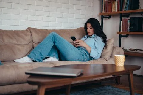 Woman using a smartphone while relaxing on the couch at home Stock Photos