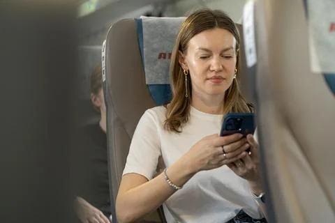 Woman Using Smartphone While Seated in a Train During Daytime, Focused on the Stock Photos