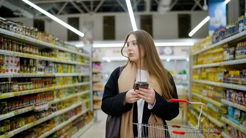 Woman using smartphone while shopping in grocery store aisle with cart Photos
