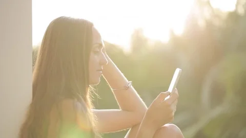 Woman using smartphone while sitting on terrace with garden on background Stock Footage 73415337