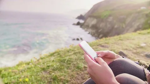 Woman Using Smartphone While Sitting On Mountain By Sea Stock Footage 79658196