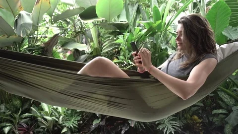 Woman using smartphone while sitting on hammock, exotic background Stock Footage 84817787