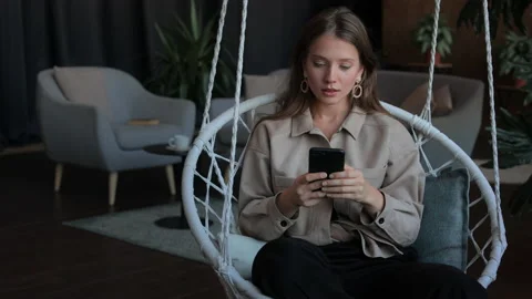Woman using smartphone while sitting in hanging chair 動画素材 172524497