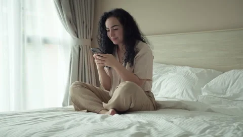 Woman using smartphone while sitting on bedroom. Using app on cellphone at home Stock Footage 241748838