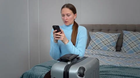 Woman using smartphone while sitting on bed with packed suitcase 库存影片 307321679