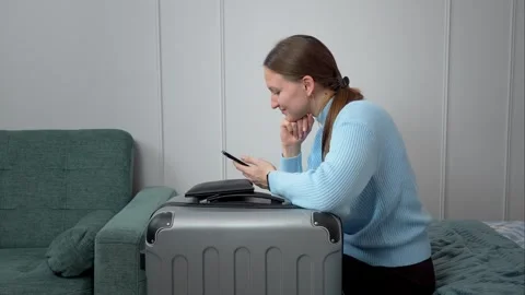 Woman using smartphone while sitting on bed with packed suitcase Stock Footage 307323198