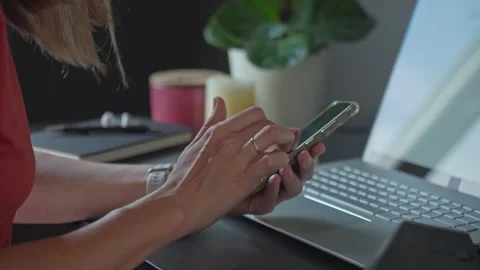 Woman using smartphone while sitting at a desk with a laptop Stock Footage 313683239