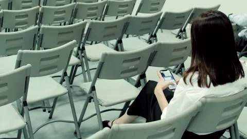 Woman using smartphone while sitting alone in empty chairs row Stock Footage 318075965