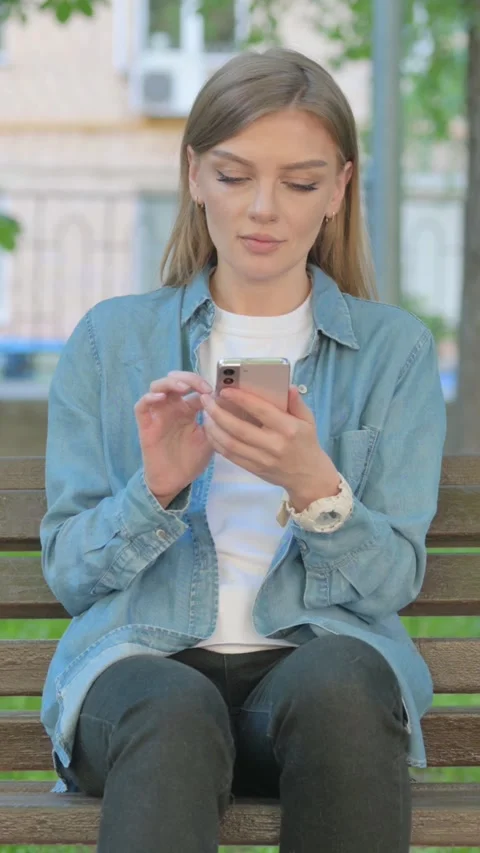 Woman Using Smartphone while Sitting on Bench in Park, Vertical Video Stock Footage 319006542